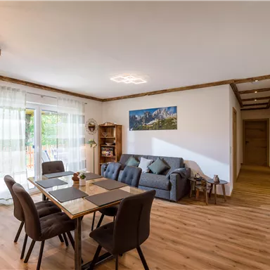 A modern living room with a dining area and a cozy sofa. Large windows provide plenty of daylight and an open atmosphere.