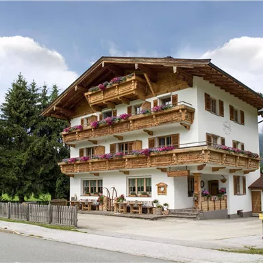 A picturesque alpine building with wooden decorations and flower balconies. Surrounded by trees and mountains, it radiates a cozy atmosphere.
