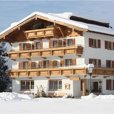 A beautiful chalet in the snow with wooden cladding and multiple balconies. Surrounded by snow-covered trees and a clear sky.
