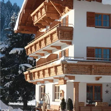 A picturesque house in Alpine style, surrounded by snow. The sun is shining on the wooden building and the adjacent landscape.