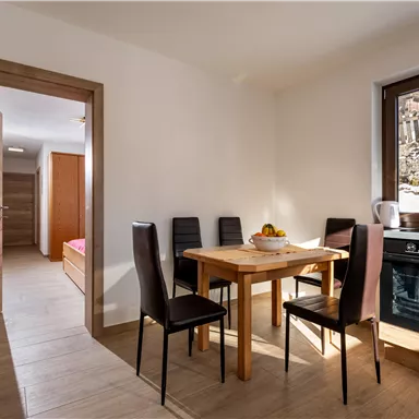 A bright and modern kitchen with a dining table and chairs. In the background, there is a window overlooking a tranquil landscape.