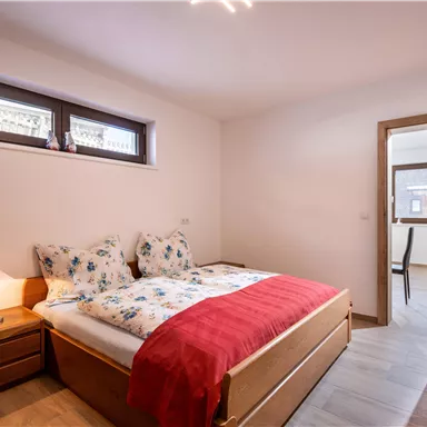 A bright bedroom with a double bed and pretty bedding. There is a wooden wardrobe and a window with daylight.