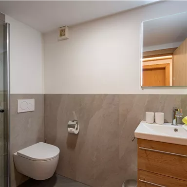 A modern bathroom with a shower and a large mirror. The white and gray tones are complemented by yellow towels.