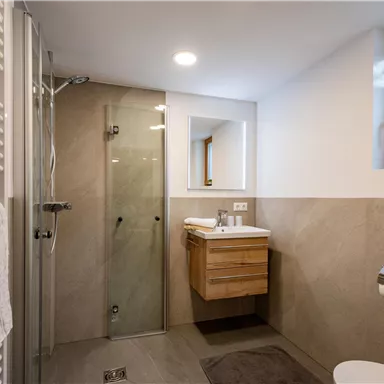 A modern bathroom with a glass shower and a wooden vanity. Bright walls and a window provide a pleasant atmosphere.