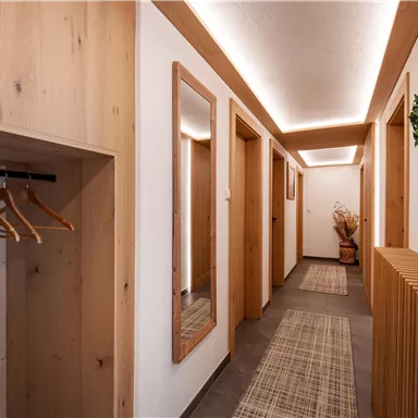 A modern hallway with wooden paneling and bright lighting. Mirrors and a decoration of plants hang on the wall.