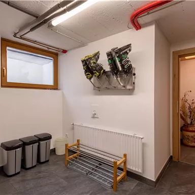 A modern entrance area with a coat rack and trash bins. Various items are hanging on the wall, and a door leads to another room.