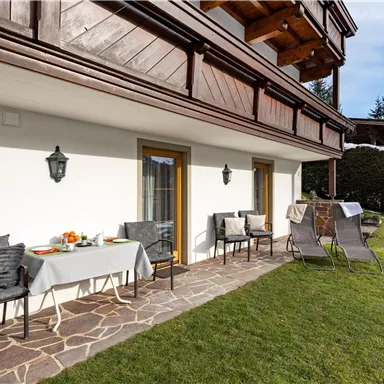 A cozy terrace with garden furniture and a table set for breakfast. In the background, green meadows and trees are visible.