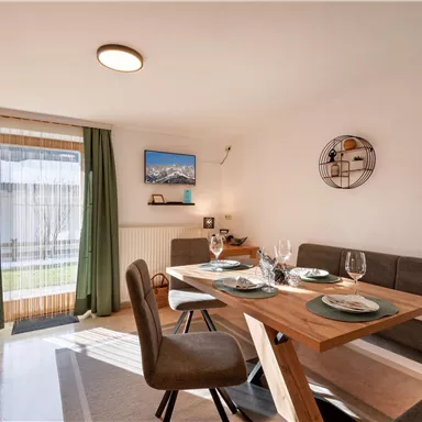 A bright dining room with a wood-colored table and comfortable chairs. The windows let in plenty of light and offer a view of the outdoor area.