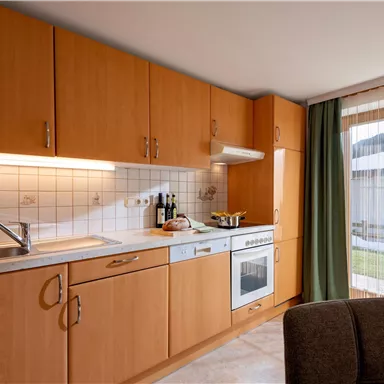 A modern kitchen with wooden cabinets and a bright countertop. The window lets in plenty of daylight and offers a view of the outdoor area.