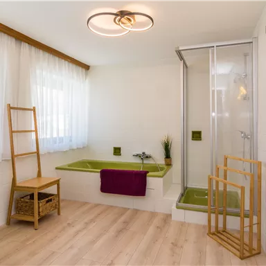 A modern bathroom with a shower cabin and a cozy bathtub area. The space is bright and inviting, designed with wood and green tones.