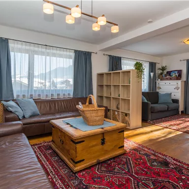 A cozy living room with a brown couch and a wooden coffee table. The room has large windows and a beautiful view of the mountains.