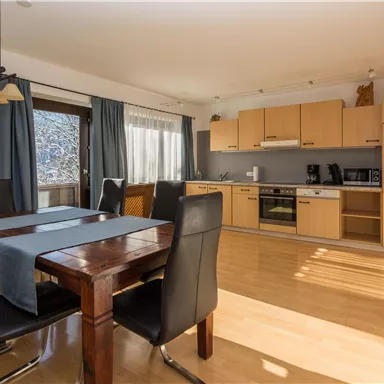 A modern kitchen with a dining table and chairs. The room is bright and cheerfully furnished.
