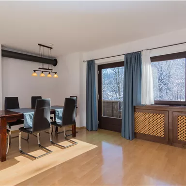 A modern dining area with a table and six chairs. Large windows let in plenty of daylight.