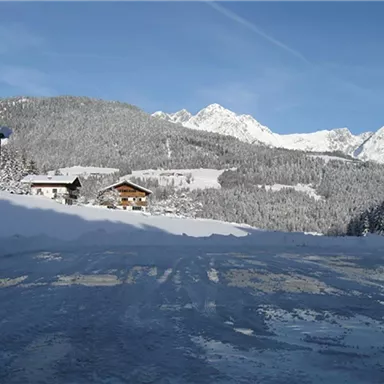 A snowy landscape with snow-covered mountains in the background. In the foreground, two cabins are visible, surrounded by freshly fallen snow.