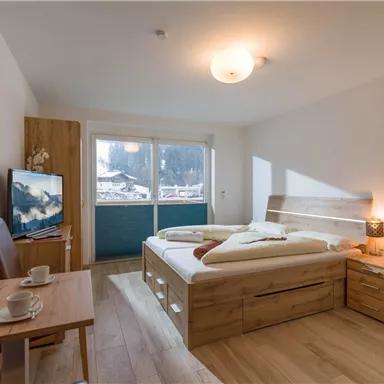A cozy bedroom with a large double bed and light wooden furniture. A table with two cups and a television are also available.