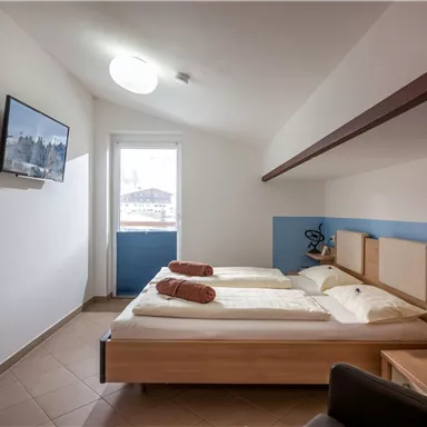 A bright room with two beds, a television, and a view out the window. The decor is modern and simple, with plants and decorative elements.