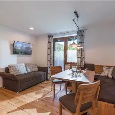 A modern living room with a dining table and cozy seating. Large windows provide plenty of light and a view outside.
