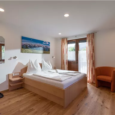 A cozy hotel room with a double bed, beautiful hardwood flooring, and a television. Large windows provide light and a view of the landscape.