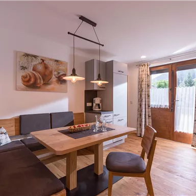 A cozy dining area with wooden chairs and a table. The room is bright and modern, with a window and warm light.