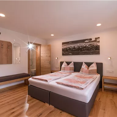 A modern bedroom with two beds and hardwood flooring. There is a television and a decorative picture wall.