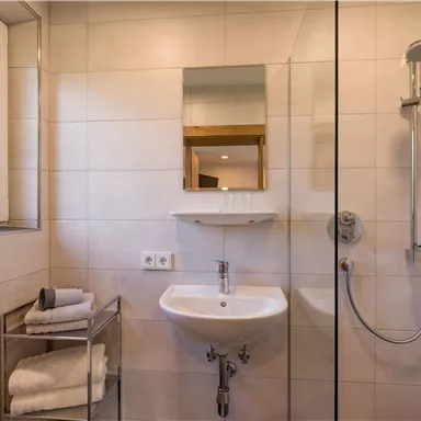 A modern bathroom with a shower and a sink. Towels are neatly arranged on a shelf.