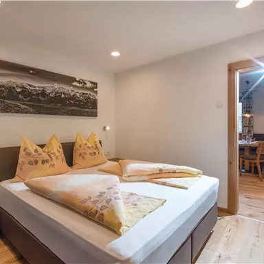 A cozy bedroom with a double bed and yellow cushions. The wooden ceilings and floor create a warm atmosphere.