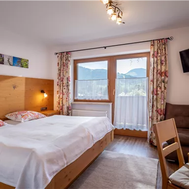 Ein gemütliches Hotelzimmer mit zwei Betten und einem Holzdekor. Große Fenster bieten einen Blick auf die Berge und sorgen für viel Tageslicht.