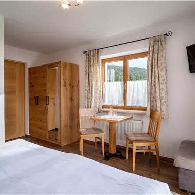 Ein gemütliches Zimmer mit Holzinterieur und einem großen Fenster. Es gibt einen Tisch mit Stühlen und einen Fernseher an der Wand.