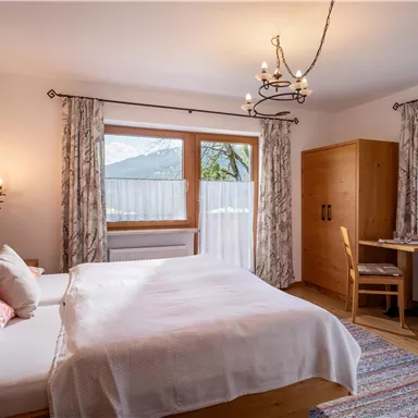 Ein gemütliches Schlafzimmer mit einem Doppelbett und holzverkleideten Möbeln. Große Fenster lassen viel Tageslicht herein und bieten einen schönen Blick nach draußen.