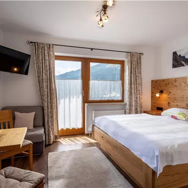 Ein modernes Schlafzimmer mit einem großen Bett und Holzmöbeln. Es gibt einen Tisch mit Stühlen und große Fenster, die einen Blick auf die Berge bieten.