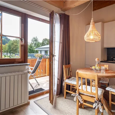 Eine gemütliche Küche mit einem runden Esstisch und vier Stühlen. Große Fenster bieten einen schönen Blick nach draußen und lassen viel Licht herein.