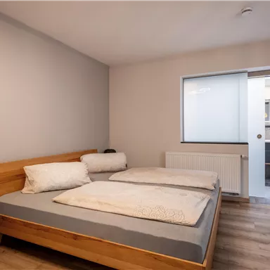 Ein gemütliches Schlafzimmer mit einem Doppelbett und Holzmöbeln. Der Raum hat ein Fenster, das Licht hereinlässt, und führt zu einem Badezimmer.