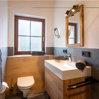Ein modernes Badezimmer mit Holzdetails und hellen Wänden. Es verfügt über ein Waschbecken, eine Toilette und ein Fenster.