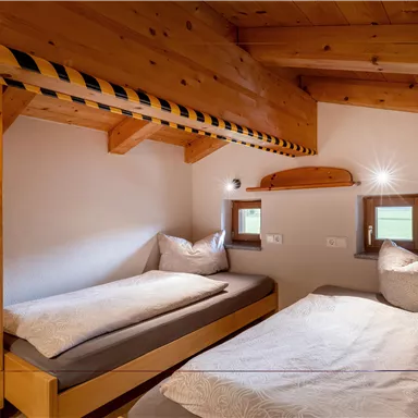 Ein gemütliches Schlafzimmer mit zwei Einzelbetten und Holzdecke. Das Zimmer ist hell und freundlich mit großen Fenstern.