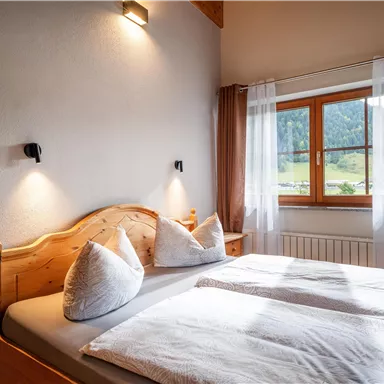 Ein gemütliches Schlafzimmer mit einem Doppelbett und zwei Kissen. Großes Fenster mit Blick auf die Natur und weichen Vorhängen.