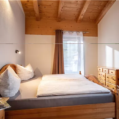 Ein gemütliches Schlafzimmer mit Holzdecken und einem Doppelbett. Neben dem Bett steht eine Kommode und der Raum ist hell und einladend.