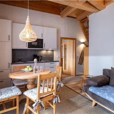 Eine gemütliche Küche mit Essbereich, Holzstühlen und einem Sofa. Der Raum hat helle Wände und einen warmen, einladenden Stil.
