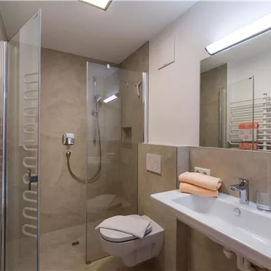 Ein modernes Badezimmer mit Dusche, Waschbecken und Handtuchheizkörper. Die Wände sind in neutralen Farben gehalten, was ein elegantes Ambiente schafft.