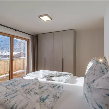 Ein modernes Schlafzimmer mit einem großen Fenster und Blick auf die Berge. Das Bett ist mit hübschen Decken und Kissen dekoriert.