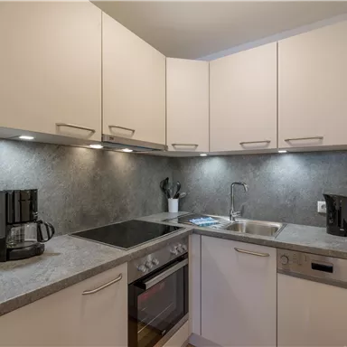 Eine moderne Küche mit hellem Design und funktionalen Geräten. Sie enthält einen Herd, einen Kühlschrank und eine Kaffeemaschine.