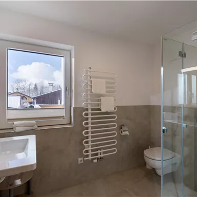 Ein modernes Badezimmer mit Dusche und großen Fenstern. Es hat helle Fliesen und eine stilvolle, schlichte Einrichtung.