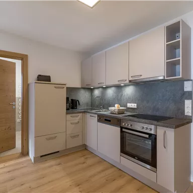 Eine moderne Küche mit hellen Schränken und einem dunklen Arbeitsbereich. Die Holzfußböden und die neutrale Farbpalette schaffen eine einladende Atmosphäre.