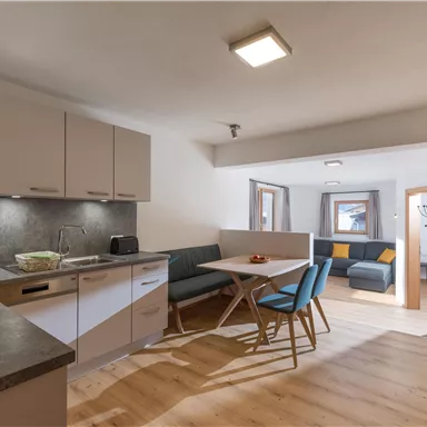Eine moderne Küche mit einem Essbereich und einem Wohnzimmer im Hintergrund. Die Einrichtung ist hell und einladend.