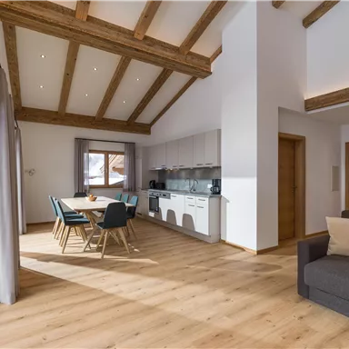 Ein modernes, helles Wohnzimmer mit Holzdecke und großen Fenstern. Es gibt einen Essbereich mit Stühlen und einen gemütlichen Platz zum Entspannen.