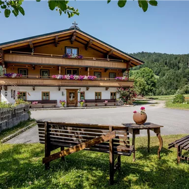 A charming Alpine house with blooming window sills. In the foreground, garden furniture stands on a green lawn.