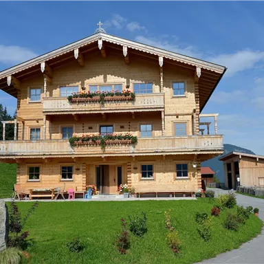 A beautiful wooden house in the mountains with a well-kept garden. The sky is blue and the surroundings are green.
