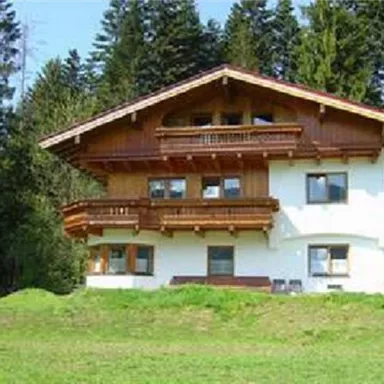 Ein schönes, traditionelles Chalet in den Bergen. Umgeben von grünen Wiesen und hohen Bäumen.