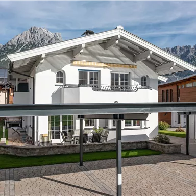 A modern house with a white facade and a landscaped property. In the background, majestic mountains can be seen.