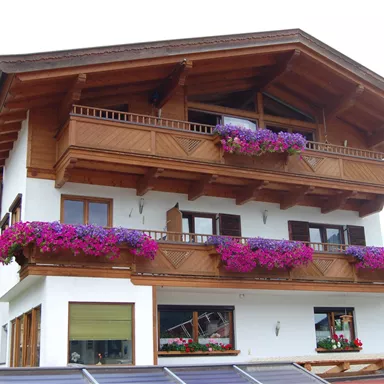 A beautiful house in Alpine style with wooden balconies and colorful flowers. The facade is designed to be bright and friendly.