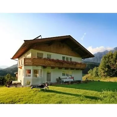 A charming house in the mountains with a balcony and green meadow. The landscape is peaceful with hills in the background.